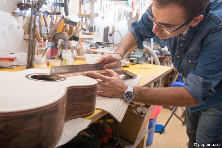 Luthier guitare Un artisan luthier prend des mesures sur une guitare en cours de fabrication.